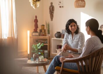 A warm, professional therapy setting with a therapist and client in conversation. The image should have soft, natural lighting and show diverse Indian individuals to represent the Indian context. The therapist should appear attentive and compassionate while the client looks engaged and comfortable, illustrating the supportive therapeutic relationship